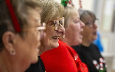 Four women are shown in profile singing wearing Christmas jumpers and accessories.